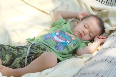 A baby boy sleeping outside on a hammock.