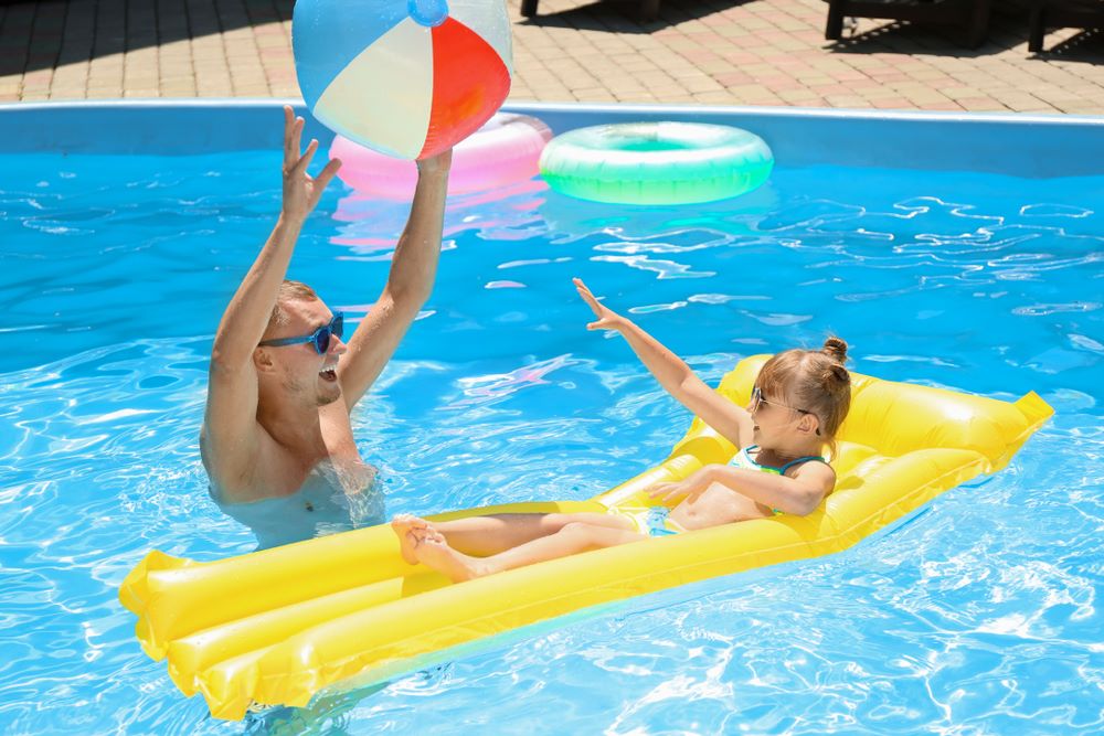 A father and child enjoying pool time with floating objects.