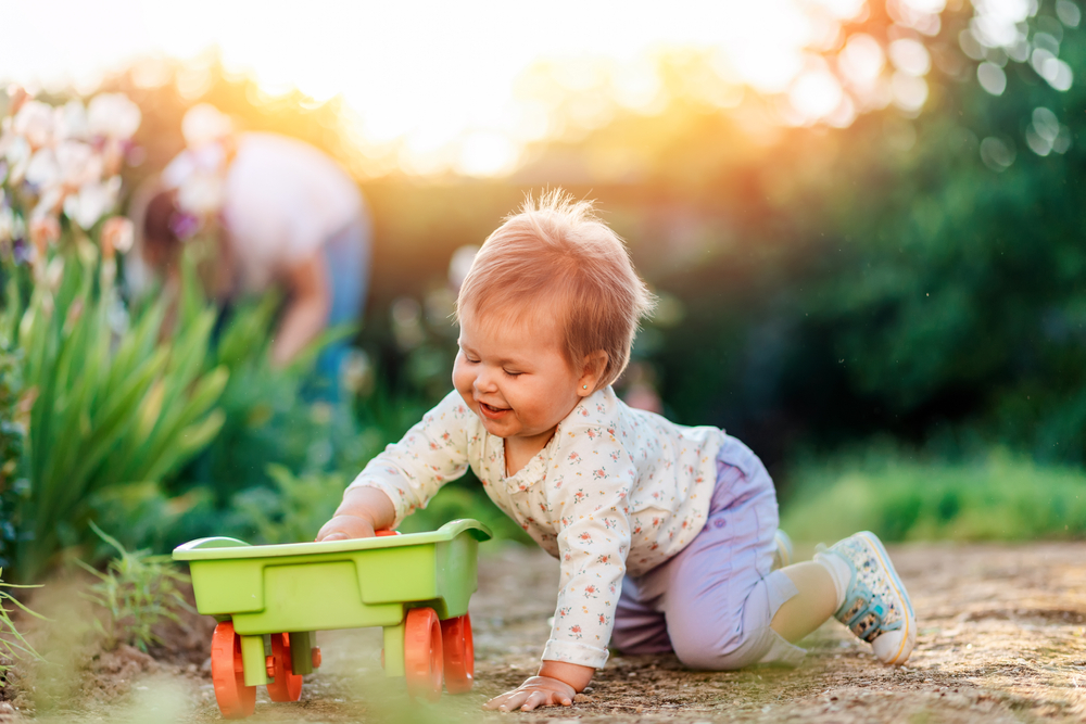 A baby playing with a green toy trailer outside.