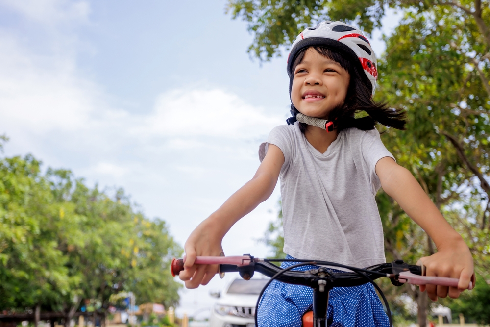 A little girl riding a bike with a helmet on.