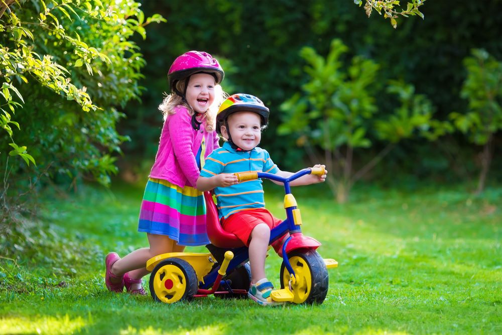 Two kids playing with a tricycle.