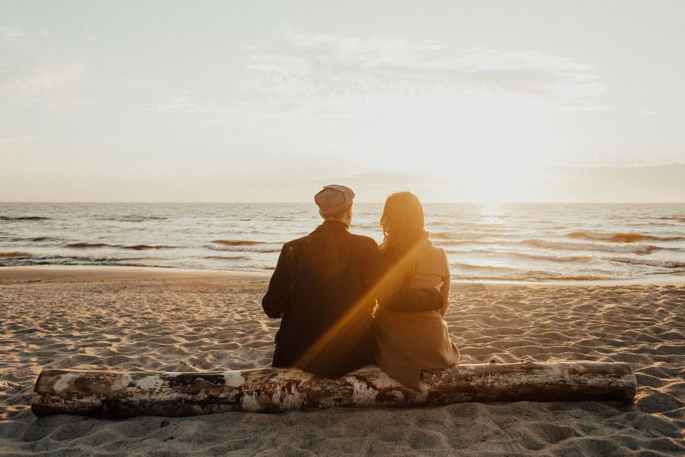 a man and woman sitting on a log on the beach