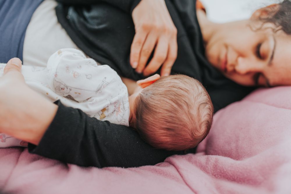 a woman is breastfeeding a baby on a pink blanket