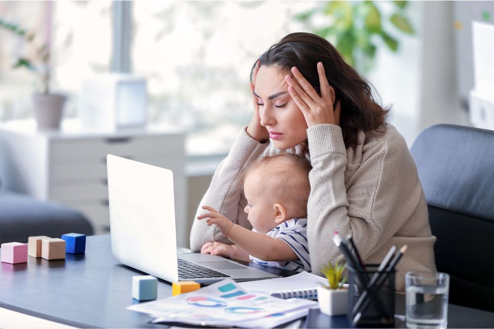 a woman holding a baby while using a laptop