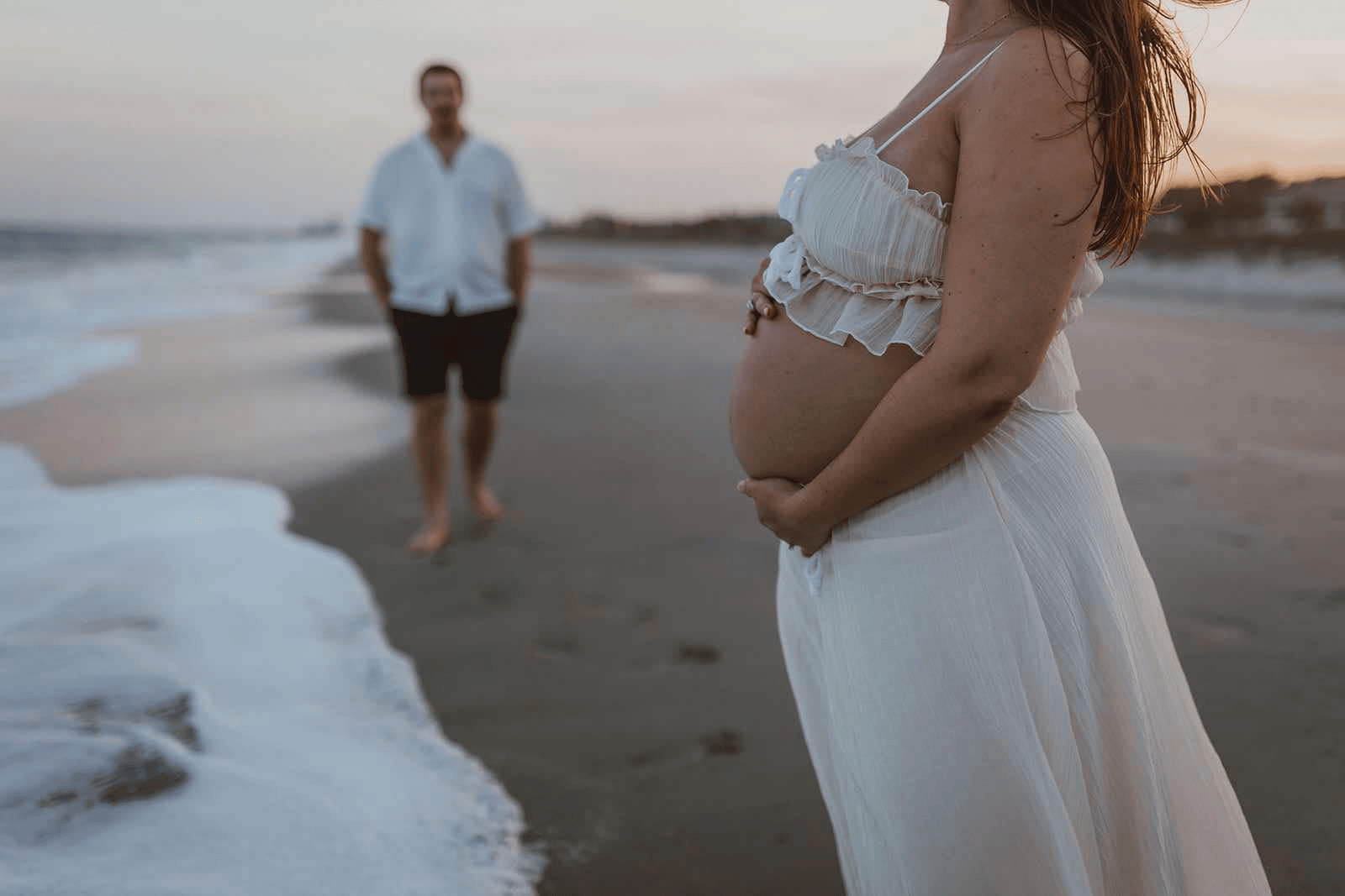 a pregnant woman standing on a beach next to a man