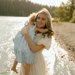 a woman holding a baby in her arms near a body of water