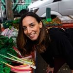 a woman smiles as she leans over a pile of vegetables