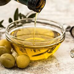 a bottle of olive oil being poured into a bowl of olives