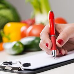 a woman's hand writing on a notepad with a red pen