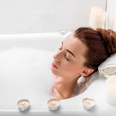 a woman laying in a bathtub with candles around her