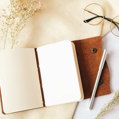 an open notebook with a pen and glasses on a table