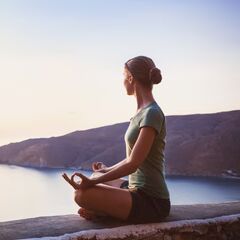 a woman sitting in a yoga position on a ledge overlooking a body of water