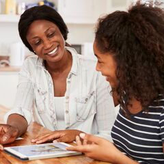 a woman and two girls sitting at a table looking at a tablet