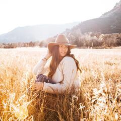 a woman wearing a hat is sitting in a field