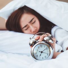 a woman laying in bed with an alarm clock