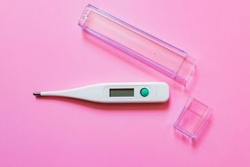 an electronic thermometer and a plastic container on a pink background