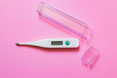 an electronic thermometer and a plastic container on a pink background