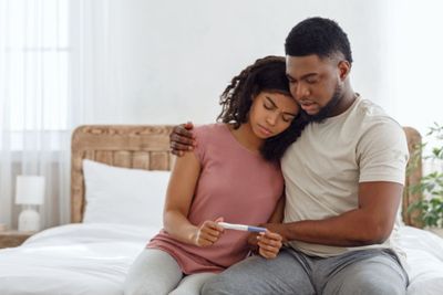 a man and woman sitting on a bed looking at a cell phone