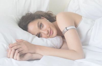 A woman in bed, wearing the Tempdrop fertility tracker.