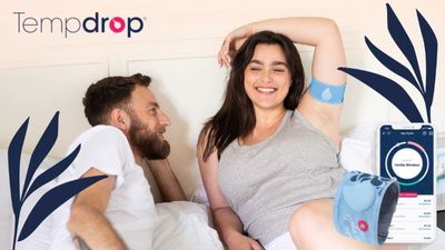 a man and a woman laying in bed, woman wearing tempdrop fertility tracker on her arm