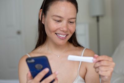 a woman holding a cell phone and a pregnancy test, monitoring results of her OPK positive but no basal body temp rise