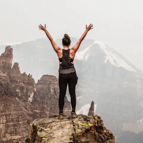 a woman standing on top of a mountain with her arms outstretched