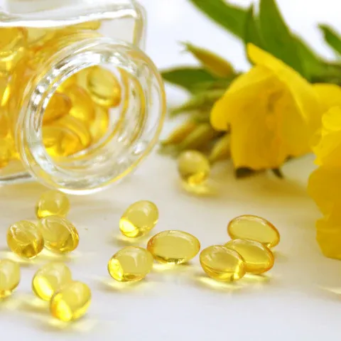 a glass jar filled with fish oil next to yellow flowers