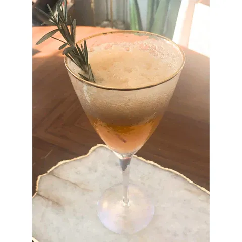 a glass filled with a liquid and a sprig of rosemary