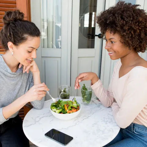 two women sitting at a table eating a salad