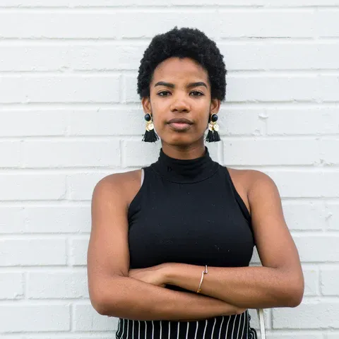 a woman standing with her arms crossed in front of a white brick wall