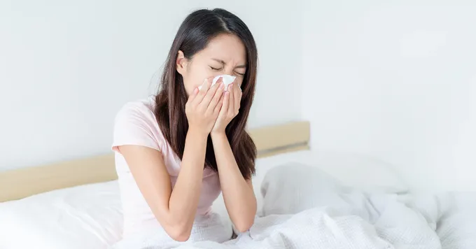 a woman sitting on a bed sneezing her nose