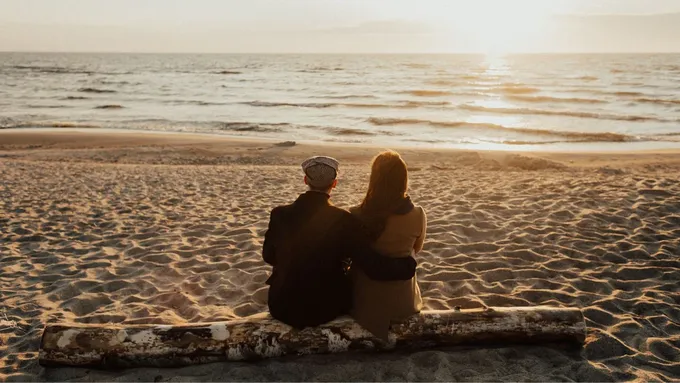 two people sitting on a log on a beach