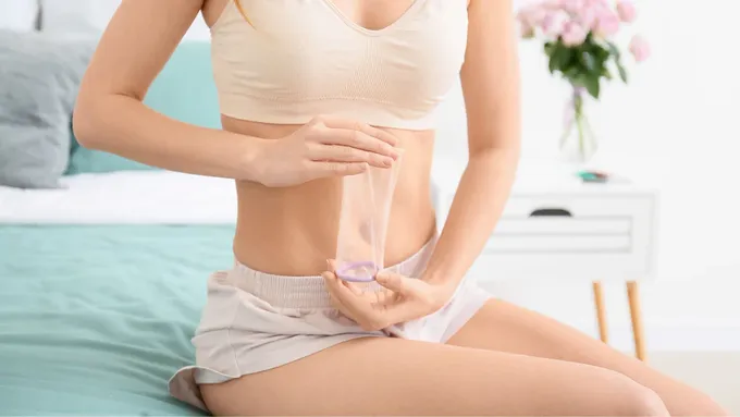 a woman sitting on a bed holding a female condom