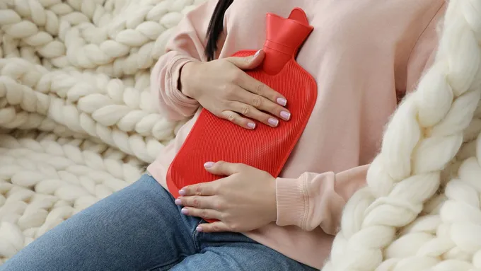 a woman sitting on a blanket holding a red bottle