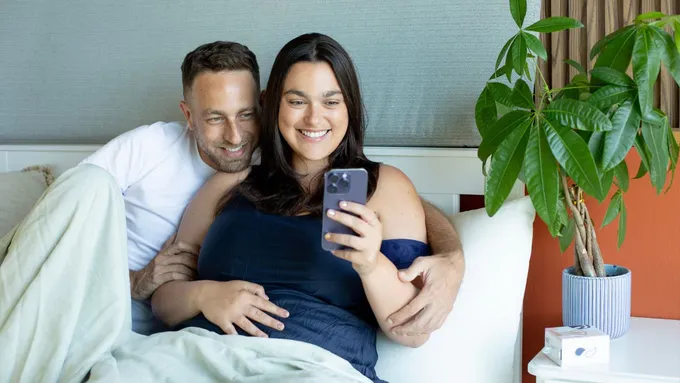 a man and woman sitting on a bed looking at a cell phone