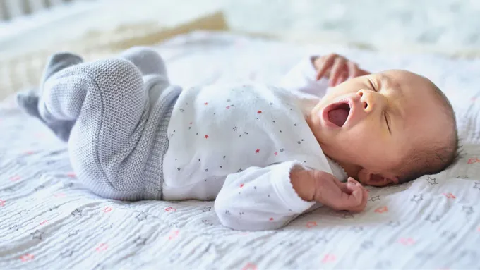 a baby yawns while laying on a bed