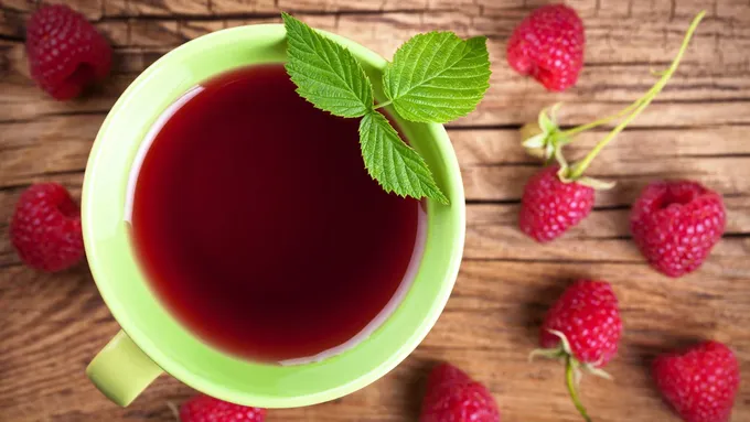 a cup of raspberry tea surrounded by raspberries