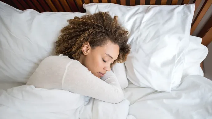 a woman sleeping in a bed with white sheets