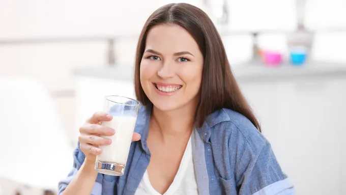 a smiling woman holding a glass of milk