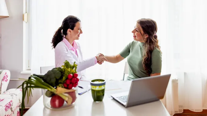 two women shaking hands in front of a laptop