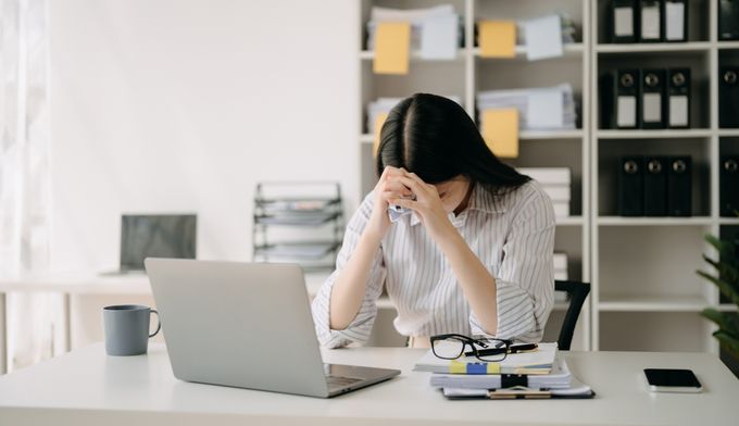 a woman sitting at a work desk in front of a laptop computer, experiencing severe period cramps at workplace