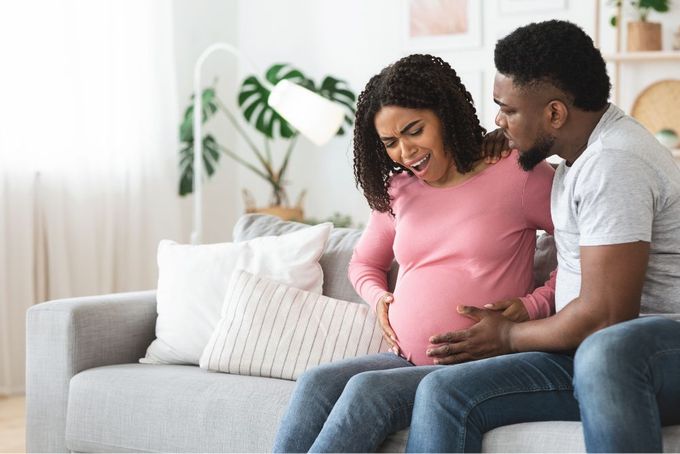 a pregnant couple sitting on a couch looking at each other