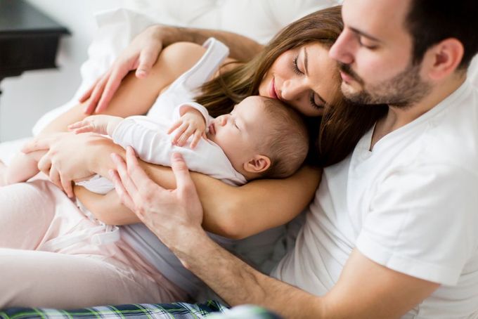 a man and a woman are laying on a bed with a baby