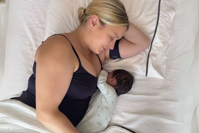 a woman laying in bed with a sleeping baby