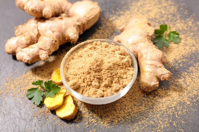 a bowl of ginger root powder next to sliced ginger