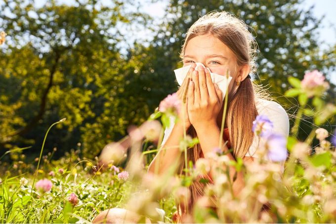 a young girl covers her mouth with a tissue in a field of flowers