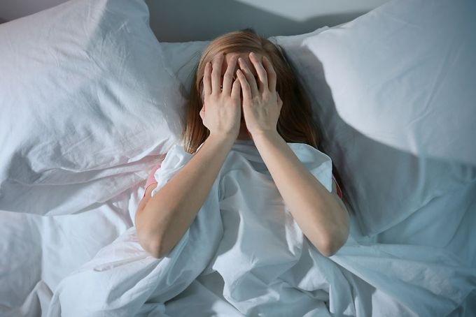a woman laying in bed covering her face with her hands