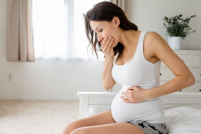 a pregnant woman sitting on a bed holding her stomach