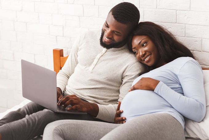 a man and woman sitting on a bed looking at a laptop