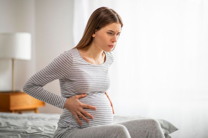 a pregnant woman sitting on a bed with her stomach exposed